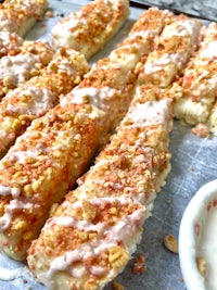 a baking sheet with a tray of bread sticks and a bowl of icing