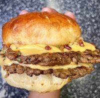 a person is holding a hamburger with cheese and bacon