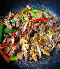 a frying pan with meat, onions and peppers